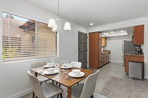 Un coin repas avec une table dressée pour quatre personnes, une cuisine équipée d’appareils modernes et une vue par la fenêtre.