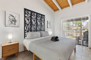 Une chambre à coucher avec un lit, une table de chevet, des œuvres d’art et une vue par la fenêtre.