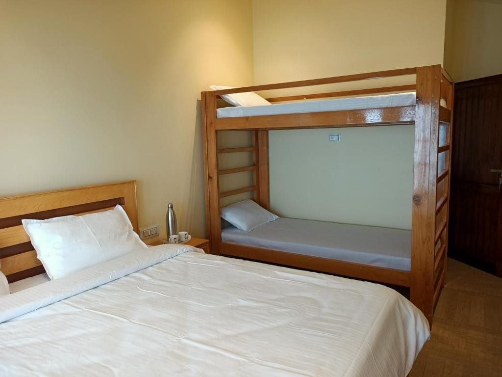 A room with a bunk bed, a single bed, and a nightstand with a lamp.