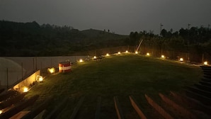 A nighttime view of a landscaped area with a grassy lawn, a small red and white structure, and a series of lights along a pathway. - Longwood Resorts (Kotagiri)