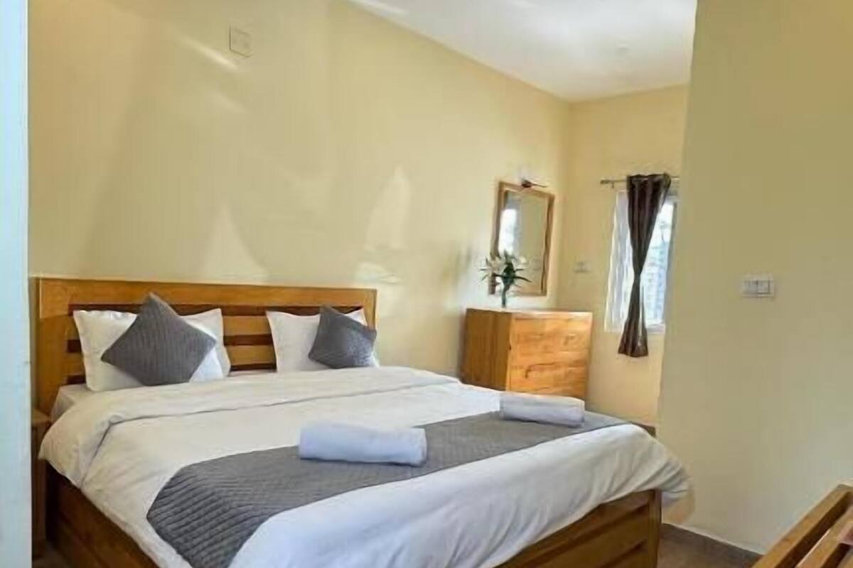 A neatly made bed with a wooden headboard, a wooden nightstand beside it, and a mirror on the wall.