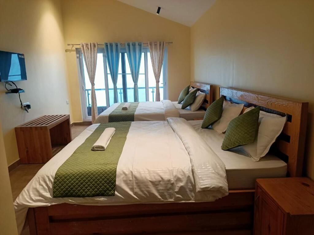 Ein Hotelzimmer mit zwei Betten, einem Fernseher und einem Fenster mit Vorhängen.