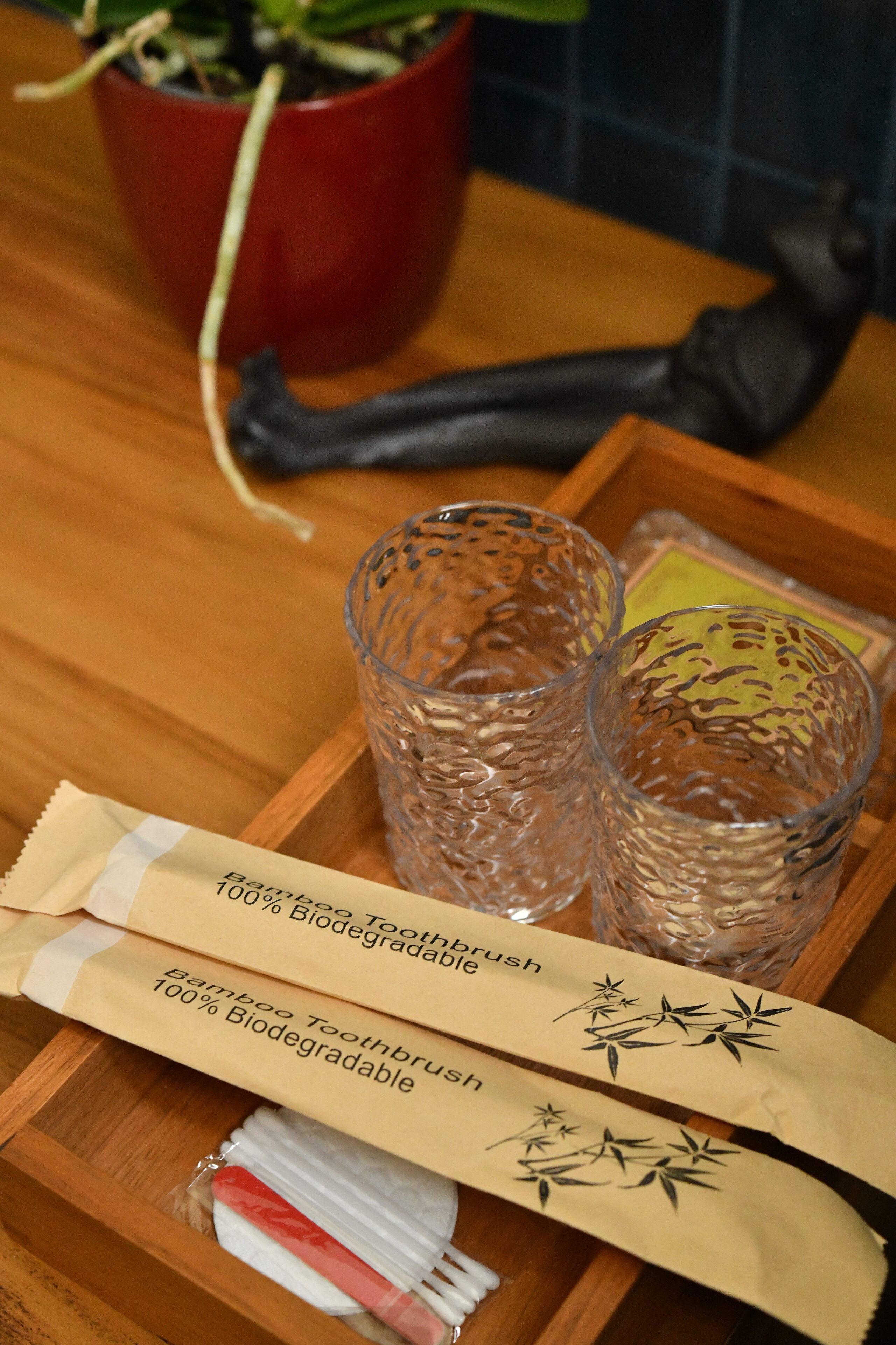A tray with two glasses, a bamboo toothbrush, and a toothbrush bag on a wooden table.