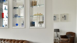 Olohuoneessa on ruskea nahkasohva, puulattia ja lasihyllyt, joilla on koriste-esineitä.
