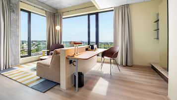 Un espacio de oficina moderno con escritorio, dos sillas, sofá y ventanas amplias que ofrecen vista a la ciudad.
