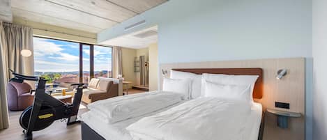 A hotel room with a large bed, exercise bike, and a view of the city.