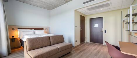A hotel room with a bed, a sofa, a desk, and a chair.