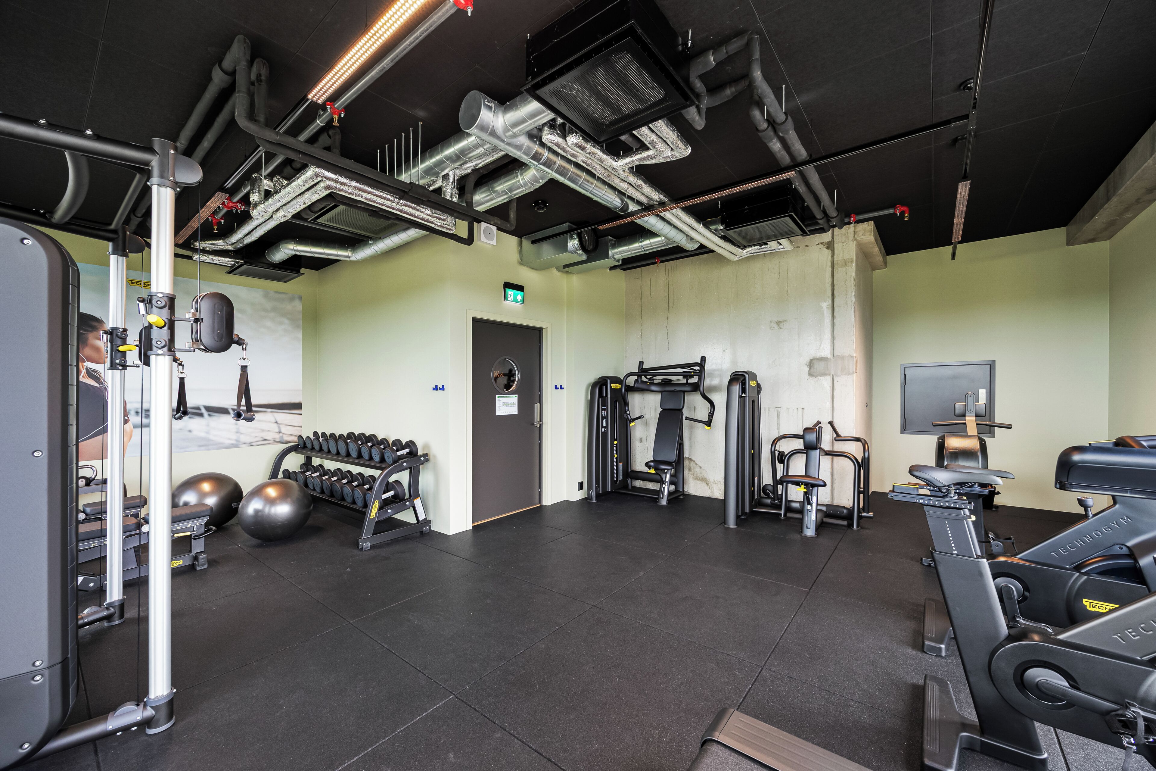 Ett gym med träningsutrustning, ett löpband och en TV som är monterad på väggen.