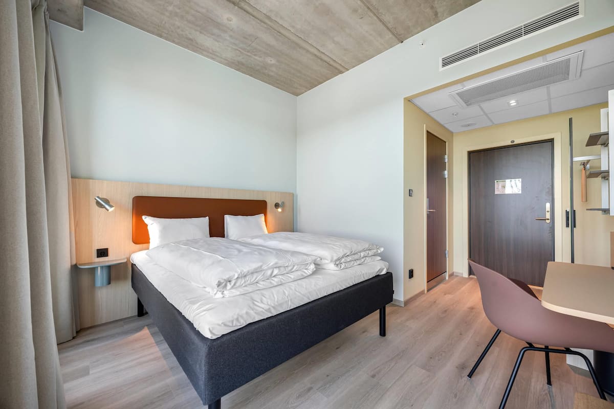 Une chambre d’hôtel comprenant un lit, une table de chevet, une lampe et un bureau avec une chaise.
