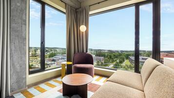 A modern hotel room with large windows, a sofa, a round table, and a chair.