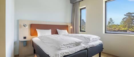 Un dormitorio moderno con cama, mesita de noche y ventana con vistas a árboles.