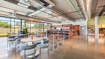 A spacious indoor area with tables and chairs, a kitchen area, and large windows offering a view of the outdoors.