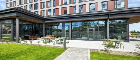 A modern building with a glass facade, outdoor seating area, and a paved walkway.