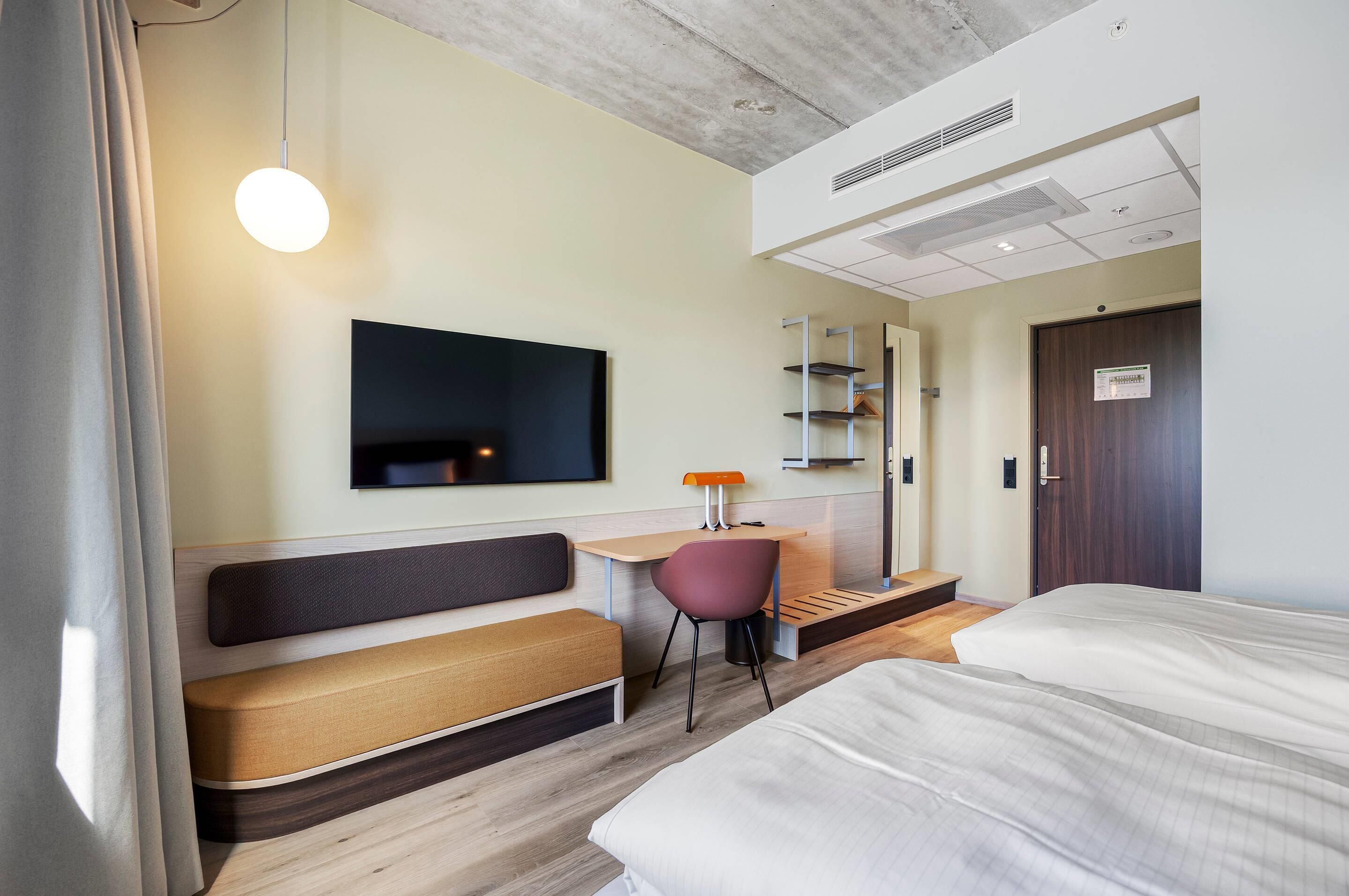 Une chambre d’hôtel comprenant un lit, un bureau avec une chaise, une télévision et une armoire.