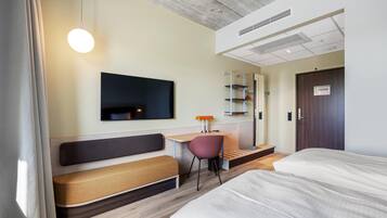 A hotel room with a bed, a desk with a chair, a television, and a wardrobe.