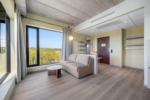 Une chambre d’hôtel moderne dotée d’une grande fenêtre, d’un canapé, d’une petite table et d’un bureau avec une lampe.