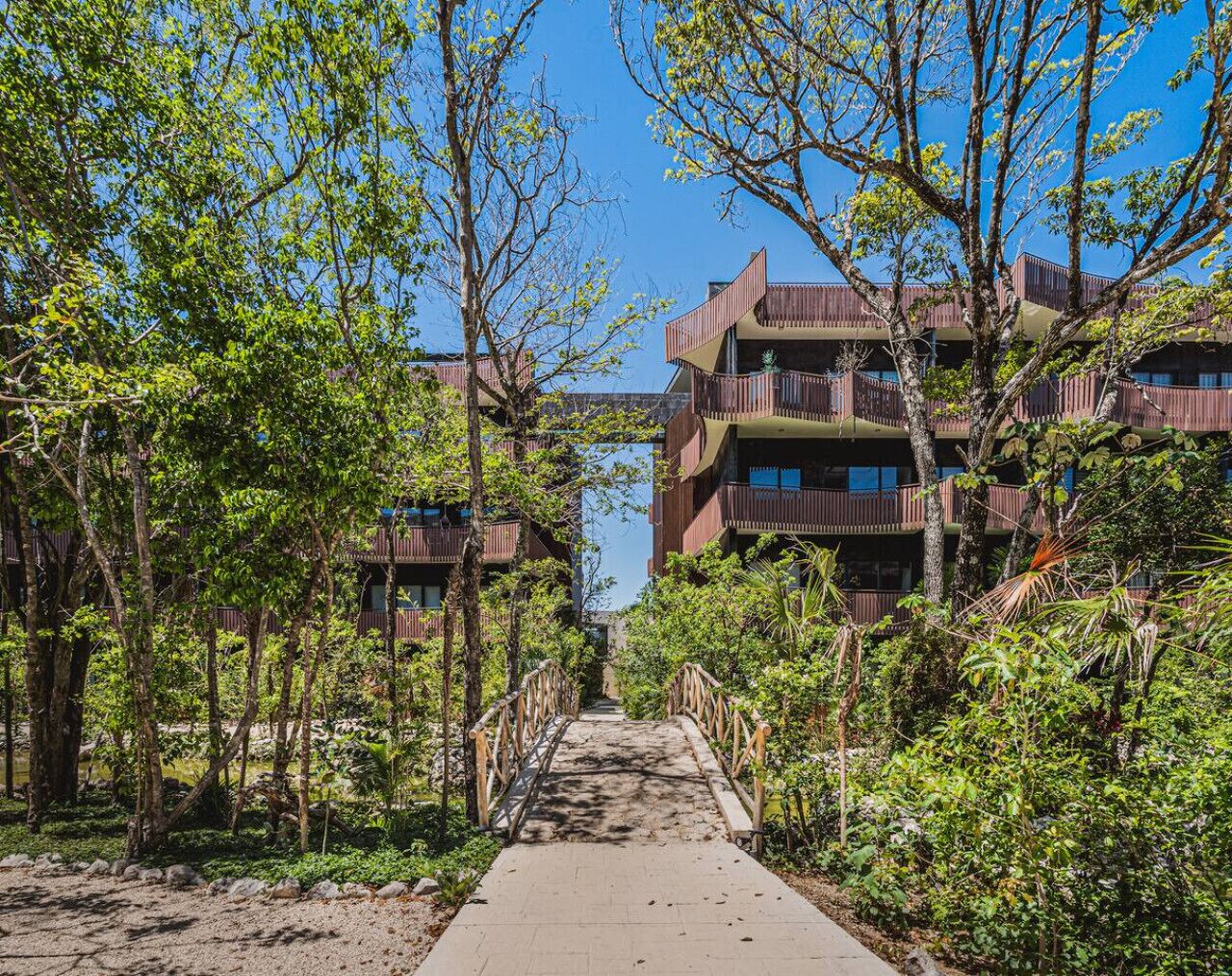Un chemin menant à un bâtiment doté de nombreux balcons, entouré d’arbres et de verdure.