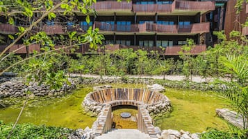 Un immeuble à plusieurs étages doté de balcons, entouré d’une végétation luxuriante et agrémenté d’une fontaine circulaire.