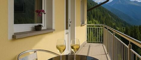 A balcony with a table set for two, featuring a glass of white wine, a plate of cheese, and bread.