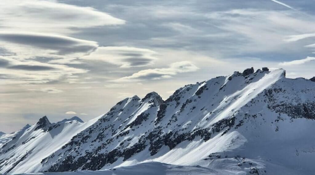 Une chaîne de montagnes enneigée, avec des pics escarpés et un ciel partiellement nuageux.