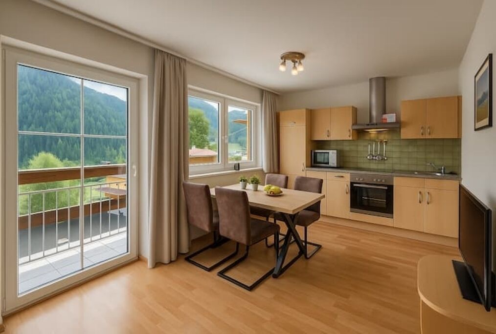 A modern kitchen with a dining area, large windows, and a view of a forested area.