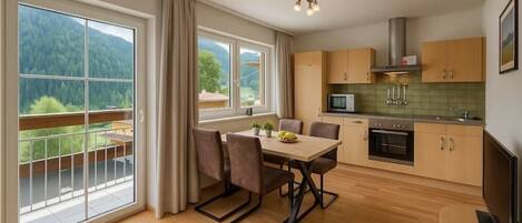 A modern kitchen with a dining area, large windows, and a view of a forested area.