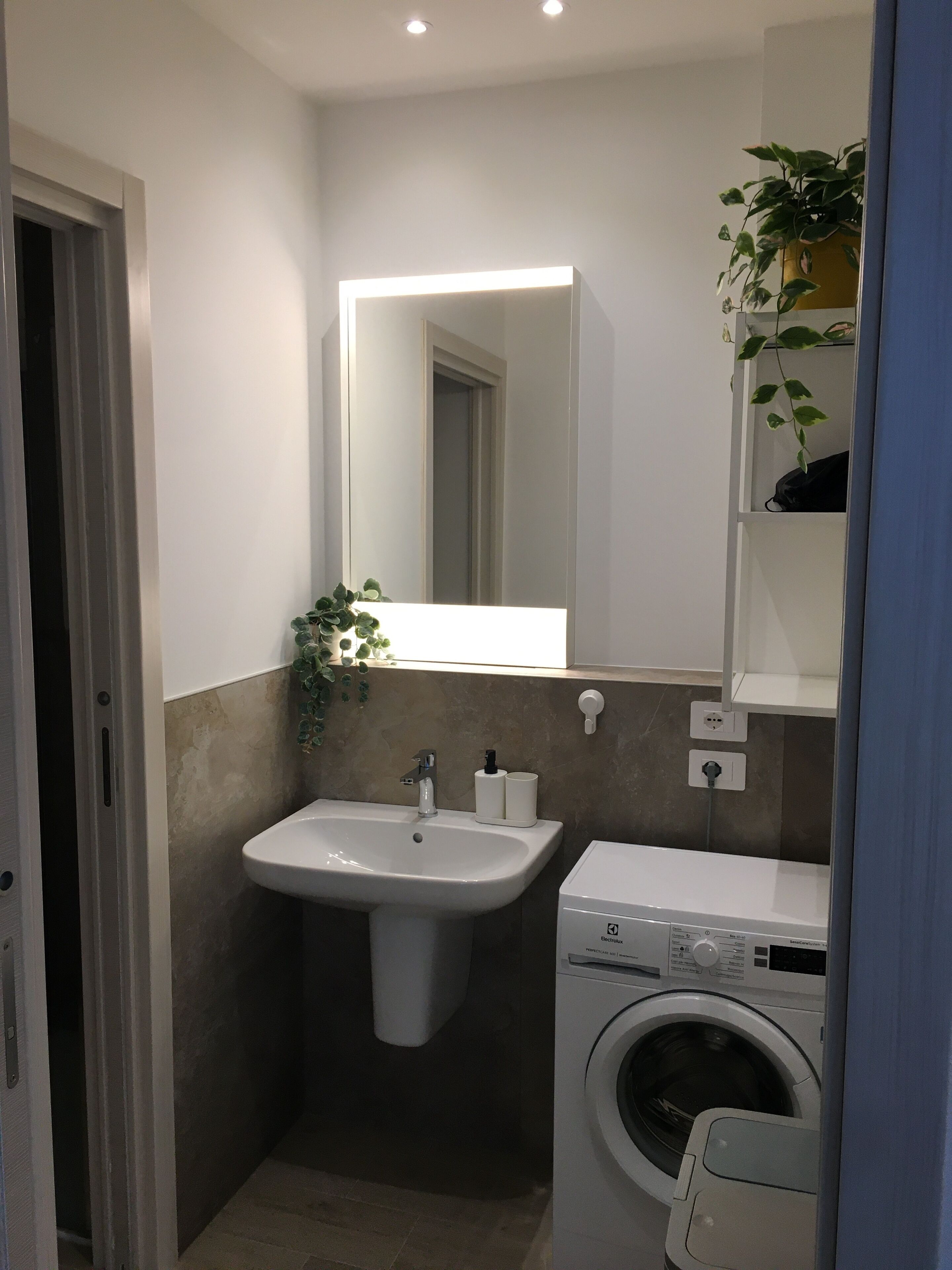 A modern bathroom with a sink, mirror, and washing machine.