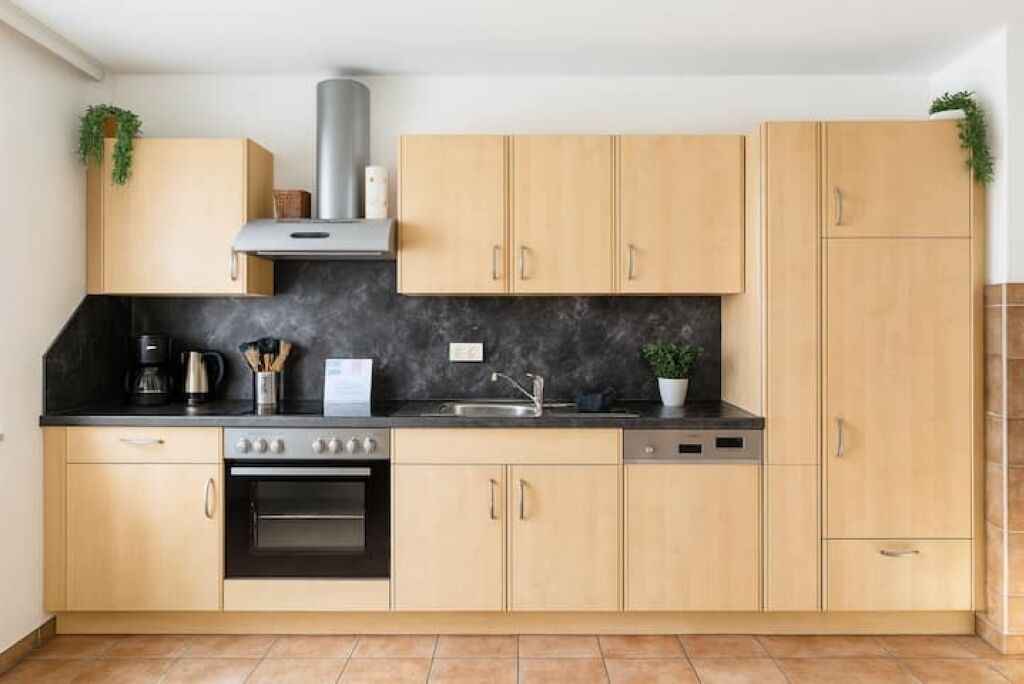Eine moderne Küche mit hellen Holzschränken, einer schwarzen Arbeitsplatte, Edelstahlgeräten und einer schwarzen Spritzschutzwand.
