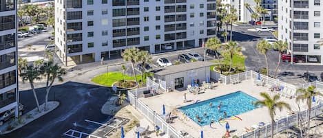 A multi-story residential building with a rooftop pool surrounded by palm trees and outdoor seating.