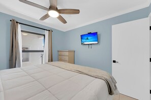 A bedroom with a bed, a ceiling fan, a television on the wall, and a sliding glass door leading to a balcony. - Estero Cove 155. Island Vacation Condo, Gulf Views, Walk to Beach! (Fort Myers Beach)
