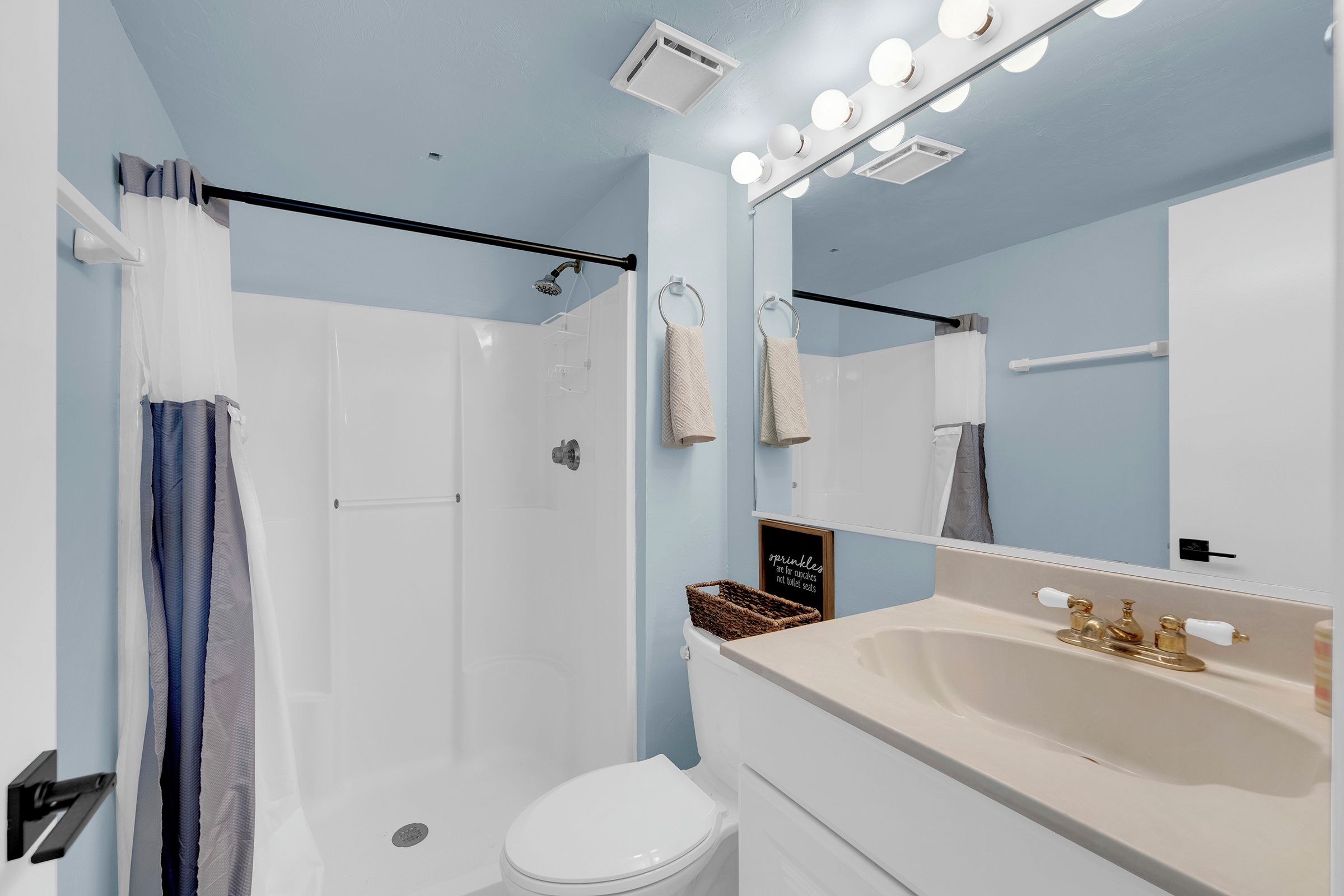 Un baño con ducha, inodoro, lavamanos y espejo con iluminación.