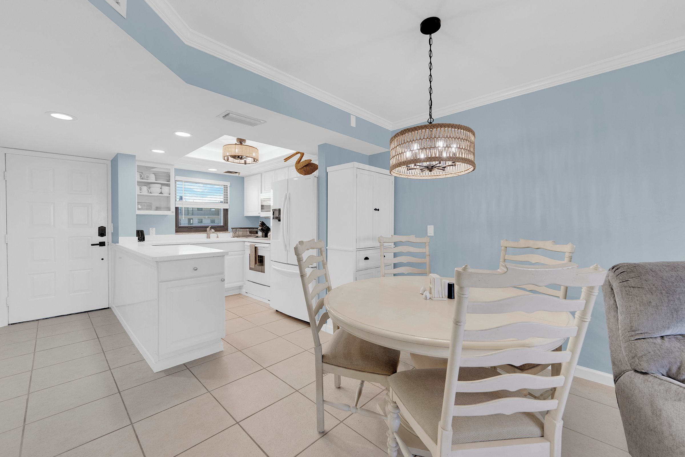 Une cuisine moderne avec des meubles blancs, un coin repas doté d’une table ronde et de chaises blanches, et un lustre.