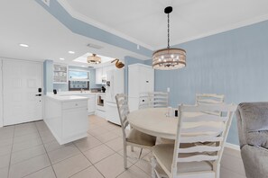 A modern kitchen with white cabinetry, a dining area with a round table and white chairs, and a chandelier. - Estero Cove 155. Island Vacation Condo, Gulf Views, Walk to Beach! (Fort Myers Beach)
