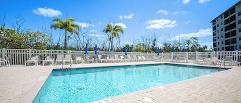 Una piscina rectangular con valla blanca y sillones de descanso alrededor.