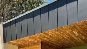 A modern building with a wooden exterior, a glass door, and a small outdoor area with a gravel path and grass. - Private coastal villa with traditional sauna located in a beautiful bush setting (Margaret River)