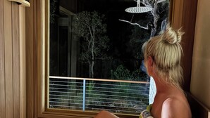 A person sitting by a window in a wooden room, with a view of trees and a railing outside. - Private coastal villa with traditional sauna located in a beautiful bush setting (Margaret River)