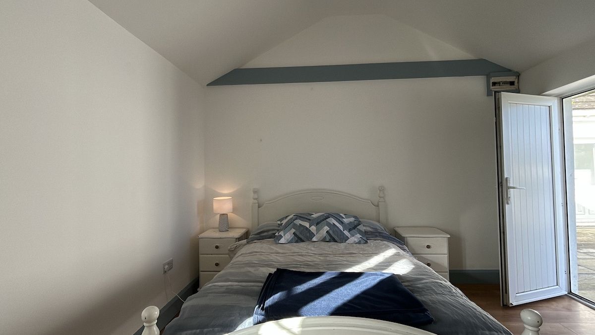 A bedroom with a bed, nightstands, a lamp, and a door leading to an outdoor area.