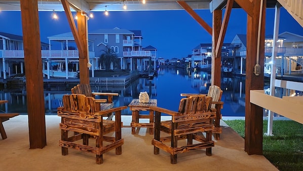 A wooden deck with two chairs and a table, overlooking a calm water body with buildings in the background.