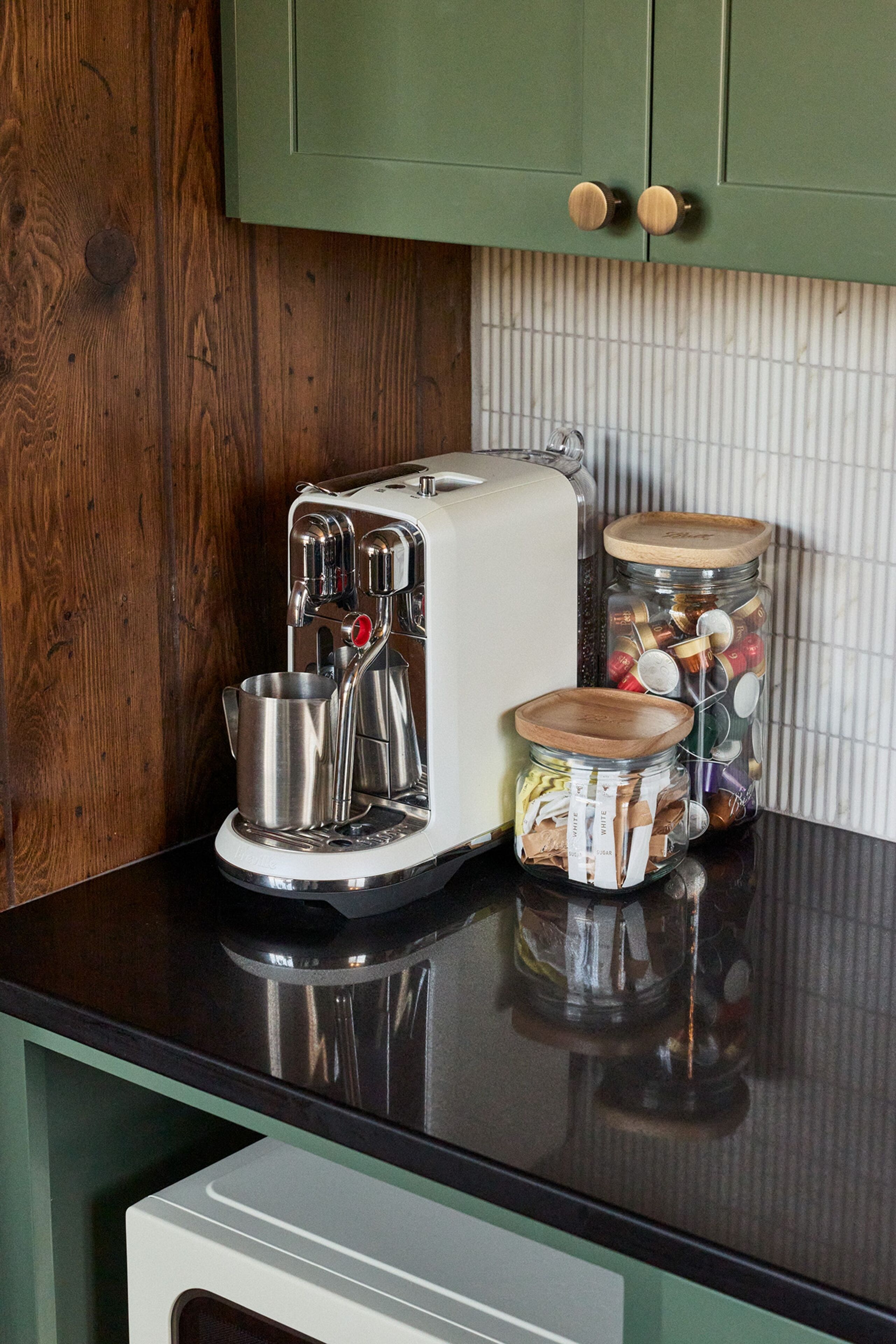 A kitchen with a coffee maker, two jars with lids, and wooden cabinets.