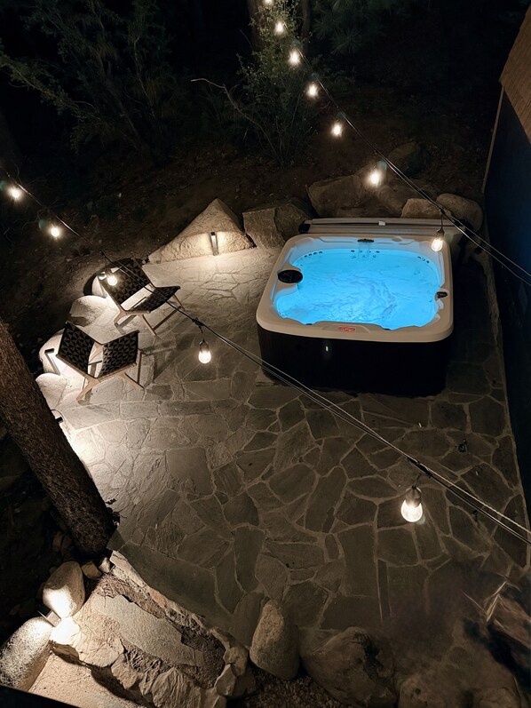 A hot tub surrounded by stone seating and a string of lights. - Basecamp Modern A Frame Retreat (Big Bear City)