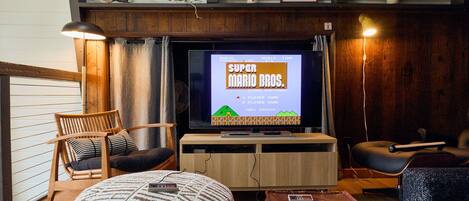 A living room with a television displaying a game, wooden furniture, and a lamp.