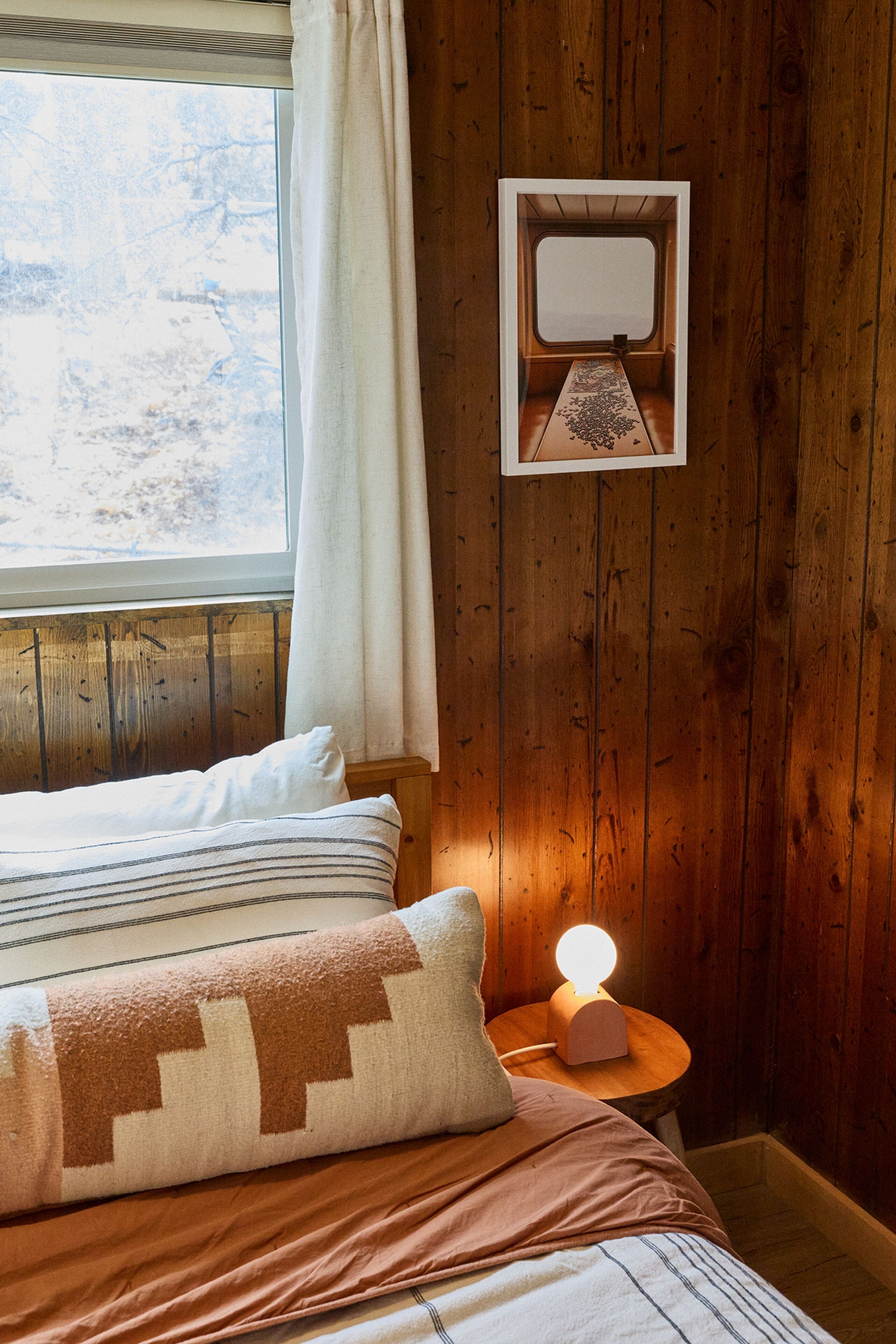 Ein Zimmer mit Holzboden, einem Bett, einem Nachttisch mit Lampe und einem Fenster mit Vorhängen.