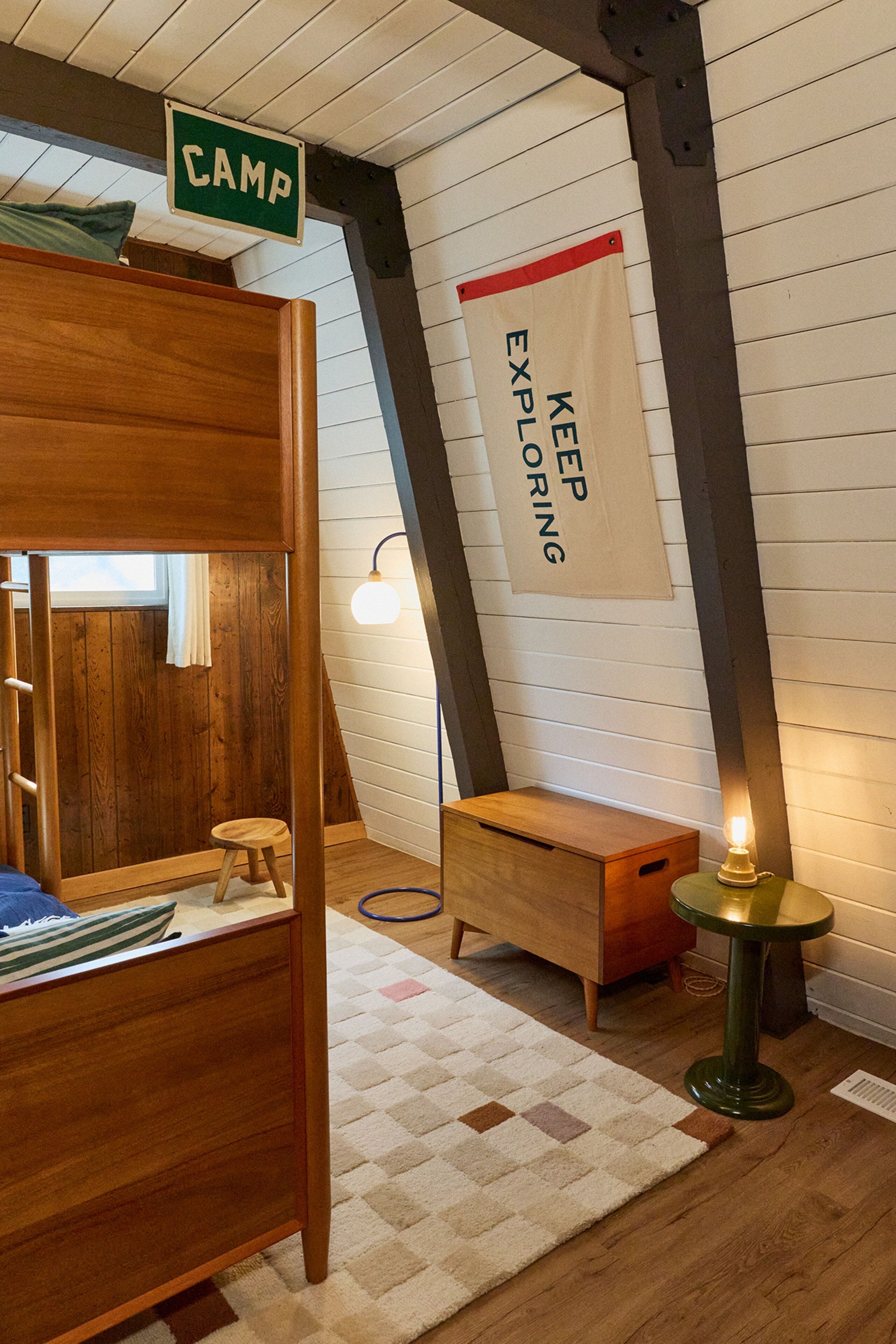 Une pièce chaleureuse avec un lit superposé, un petit bureau en bois, une lampe et une pancarte sur laquelle on peut lire : « CONTINUEZ D’EXPLORER ».