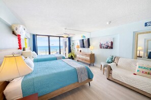 Une chambre d’hôtel avec deux lits, un canapé, une télévision, un ventilateur de plafond et une vue sur la plage.
