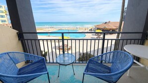 Ein Balkon mit zwei blauen Stühlen und einem kleinen Tisch, mit Blick auf einen Pool und einen Strand.