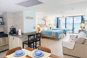 Ett modernt hotellrum med ett litet kök, två sängar, en balkong med utsikt och en matplats.
