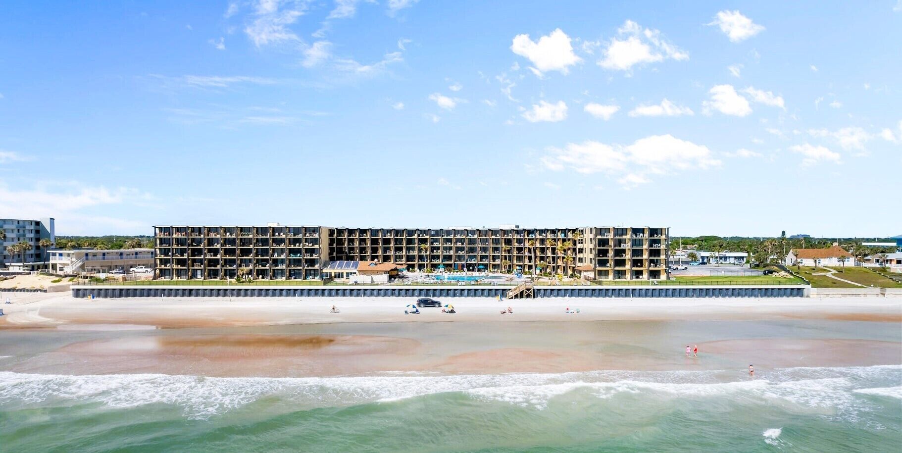 A multi-story hotel with balconies, a pool, and a beach view.