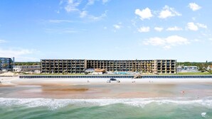 Ein mehrstöckiges Hotel mit Balkonen, einem Pool und Blick auf den Strand.