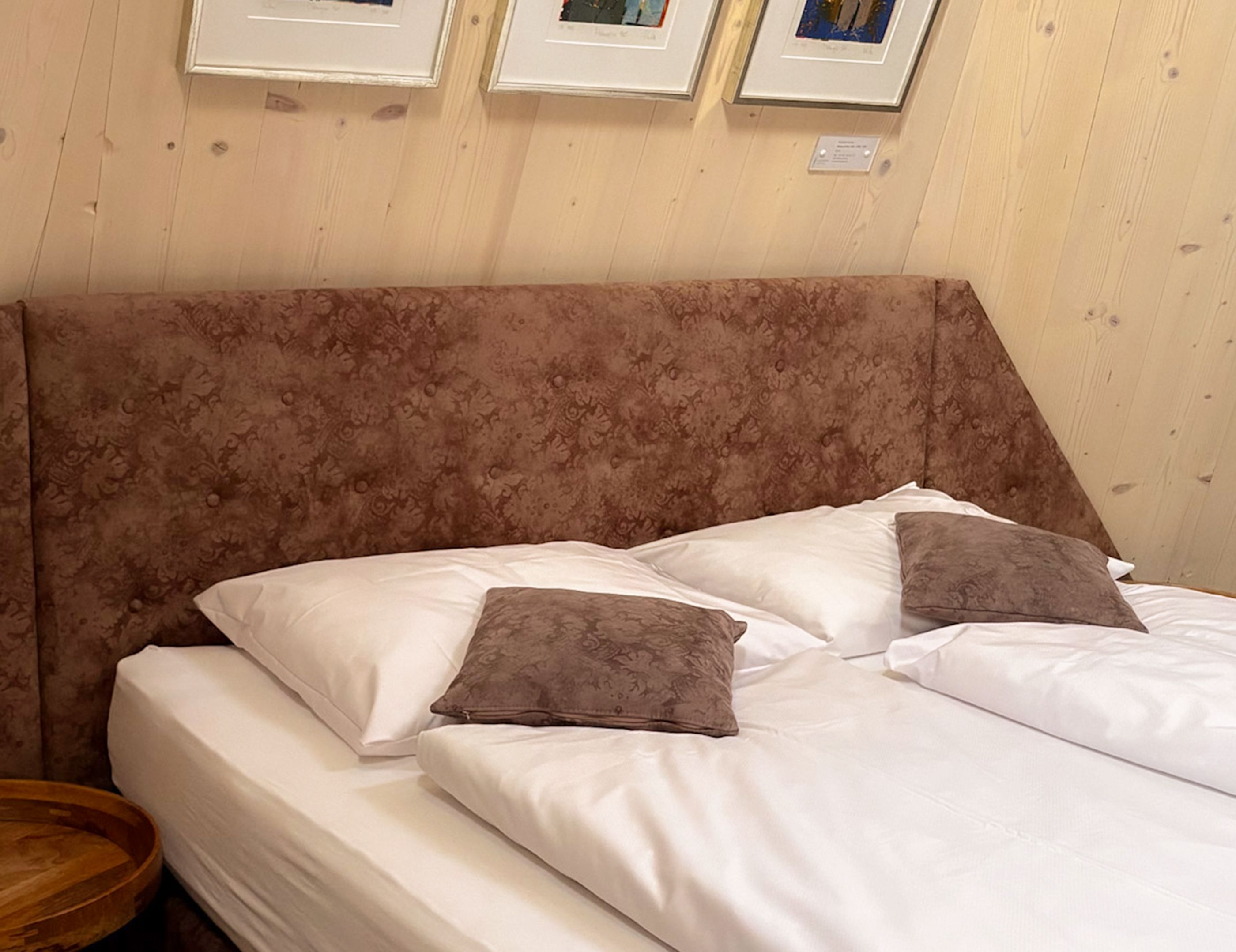A bed with white linens and two brown pillows, a wooden headboard, and a wooden side table.