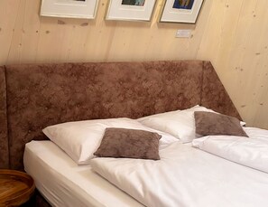 Una cama con sábanas blancas y dos almohadas marrones, cabecera de madera y una mesita de noche de madera.
